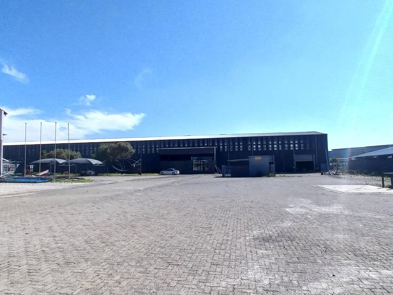 Wide-angle view of an industrial property featuring a large paved yard and multiple warehouse structures with metal cladding.