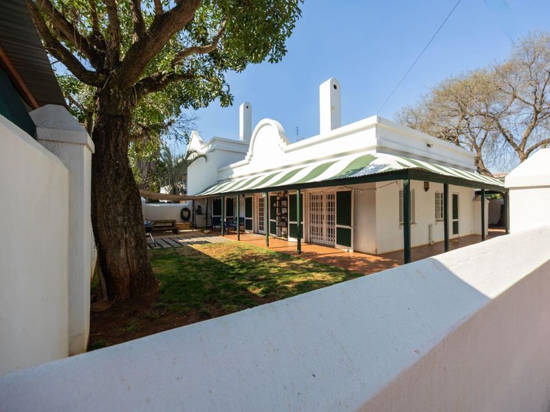 Rear view of the property featuring a covered patio with a striped awning, established garden, and traditional architectural chimneys.