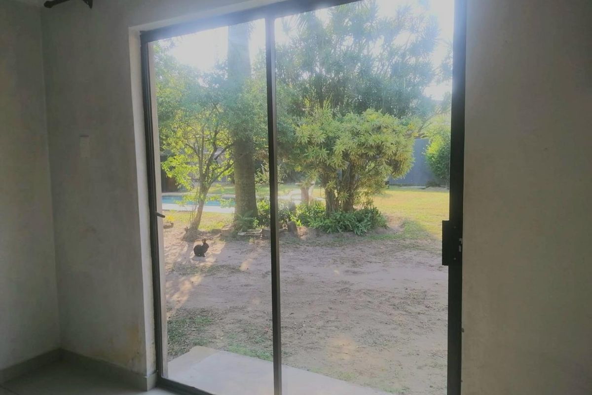 An empty living room featuring a large sliding glass door that provides direct access and views to the rear garden and pool area.