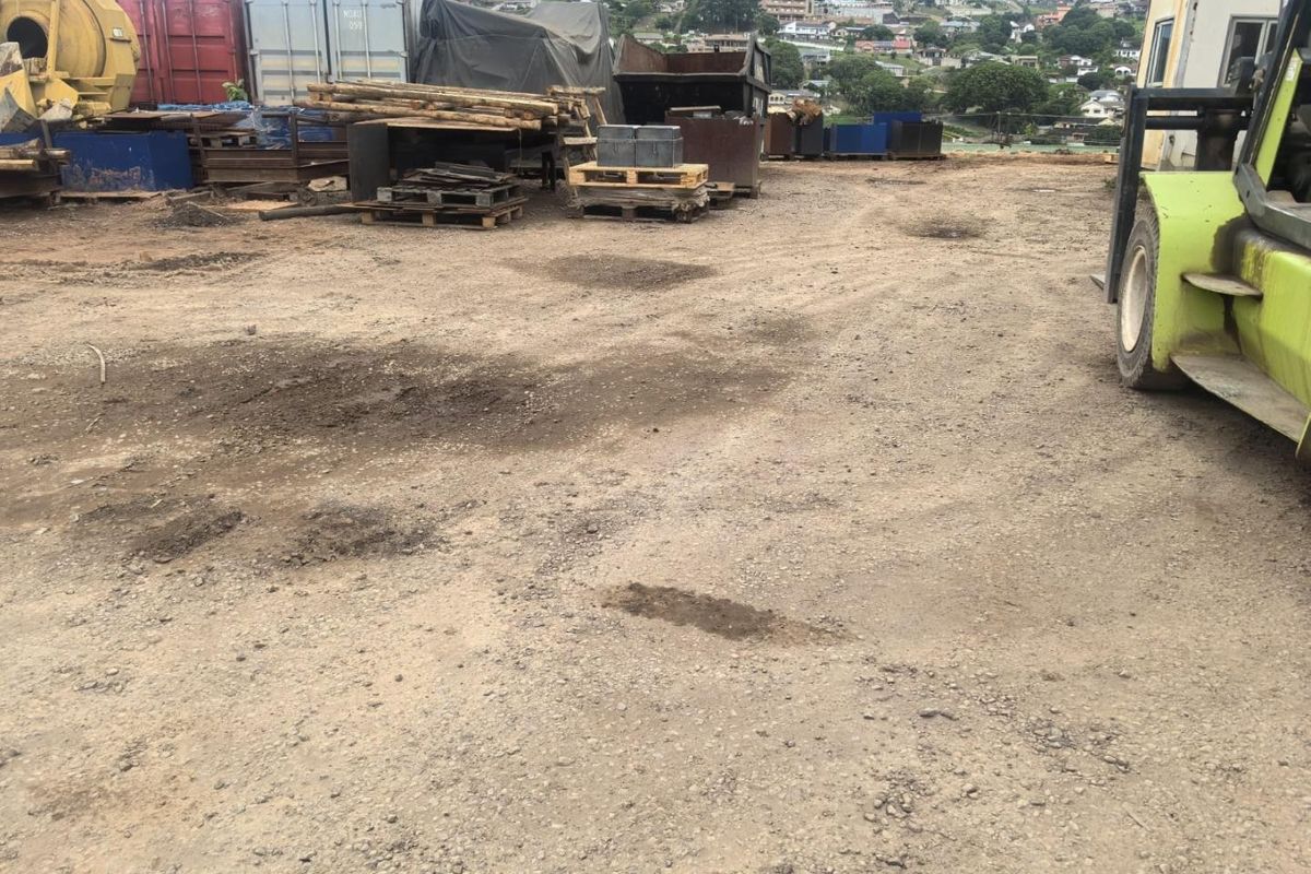 An unpaved, open utility yard area used for storage and industrial equipment, featuring uneven ground and exposed terrain.