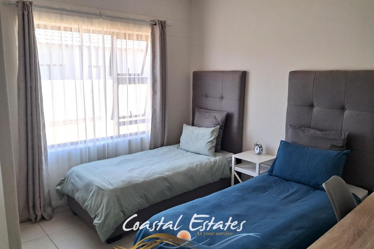 A well-maintained bedroom featuring neutral tiled flooring and a large window with fitted curtain tracks, providing ample natural light.