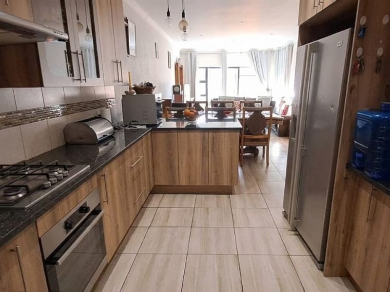 Open-plan kitchen featuring wood-finish cabinetry, granite countertops, and integrated appliances, flowing seamlessly into the adjacent dining and living area.