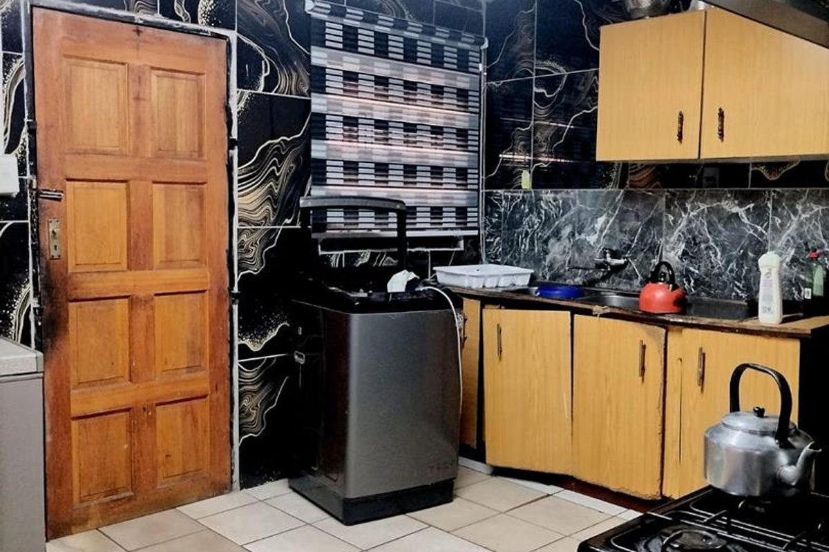 A functional kitchen featuring tiled walls, wooden cabinetry, and tiled flooring, providing a practical workspace with integrated sink and extractor fan.