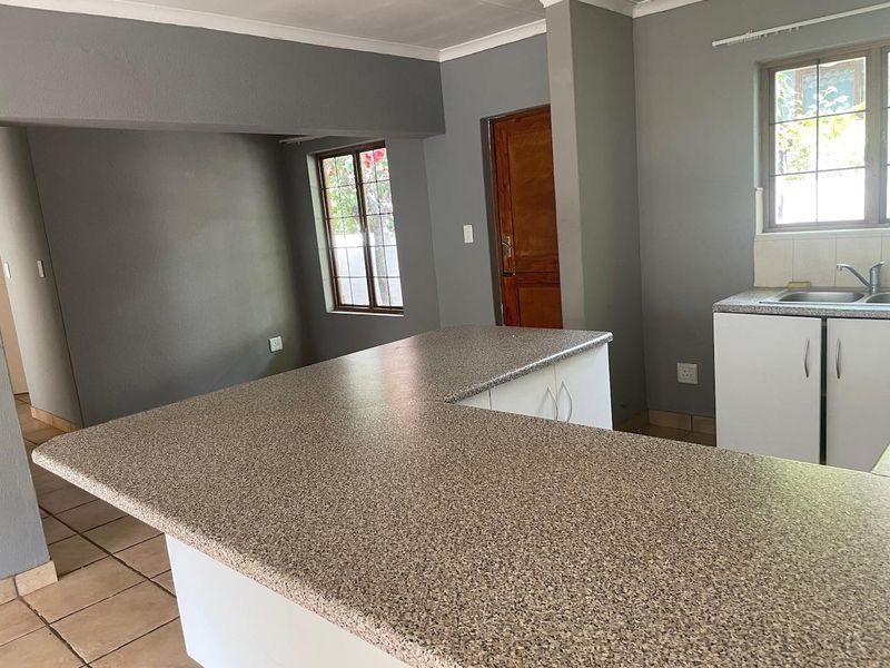 Open plan kitchen area featuring laminate countertops, built-in cabinetry, stainless steel sink, and tiled flooring in a neutral grey interior.