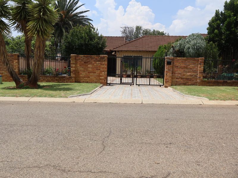 Front view of a residential property featuring a brick boundary wall, secure wrought iron gate, paved driveway, and a well-maintained garden.