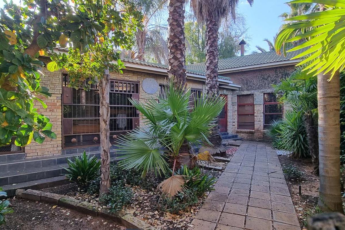 A view of the rear exterior of the house featuring brick facade, tiled walkway, and established garden landscaping.