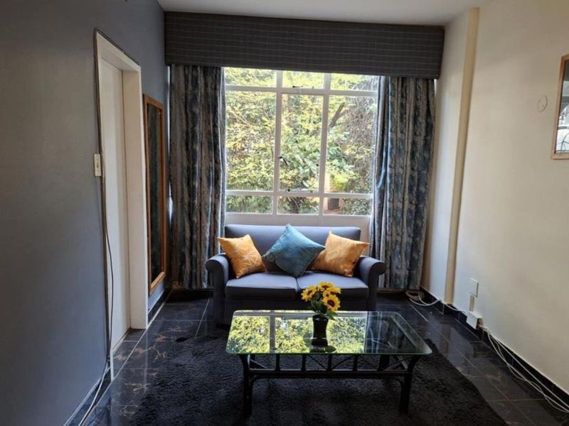 A living room featuring dark tiled flooring, a large window with a curtain pelmet, and neutral wall finishes.
