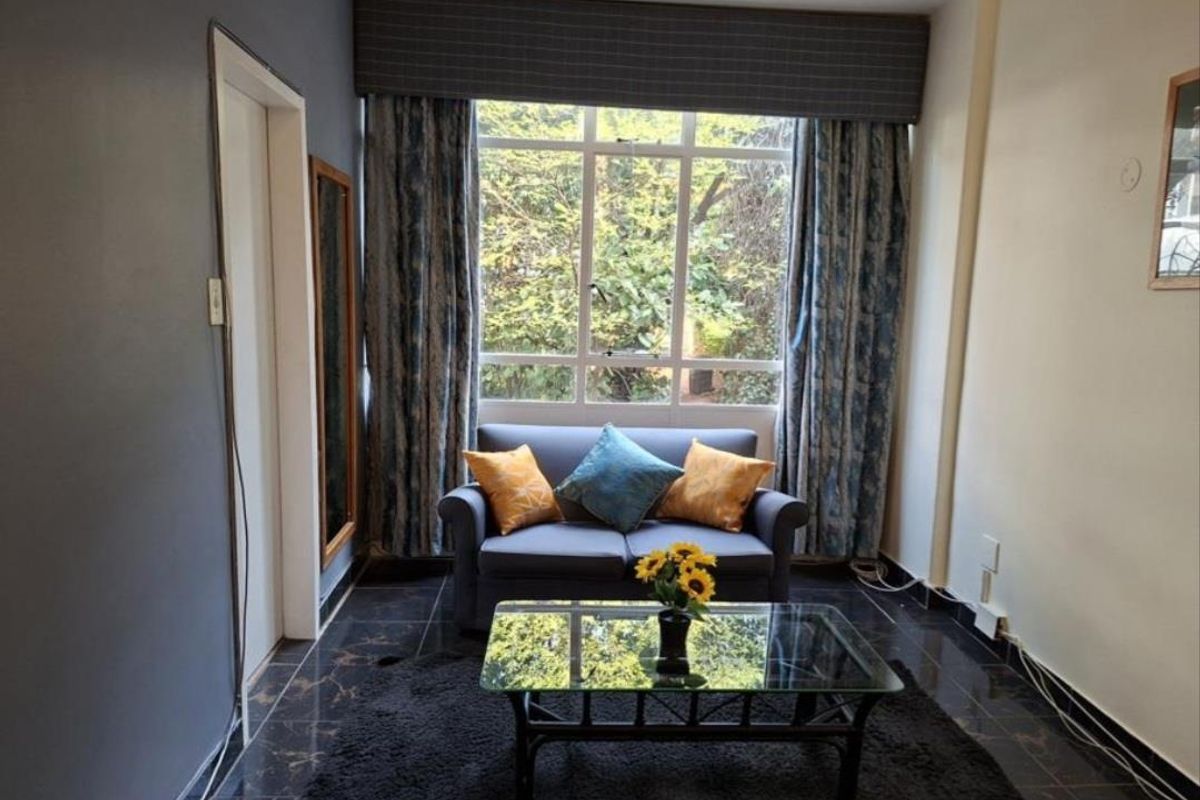 A living room featuring dark tiled flooring, a large window with a curtain pelmet, and neutral wall finishes.