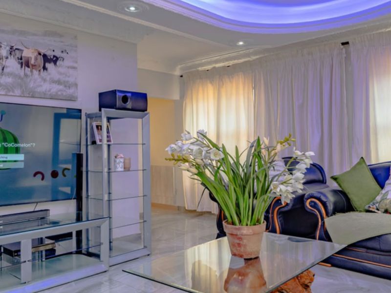 A well-maintained living room featuring decorative ceiling detailing, ambient cove lighting, and polished tiled flooring.