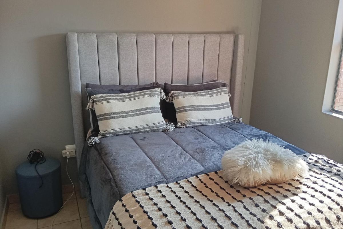 A well-maintained bedroom featuring neutral wall tones, tiled flooring, and a large window allowing natural light.
