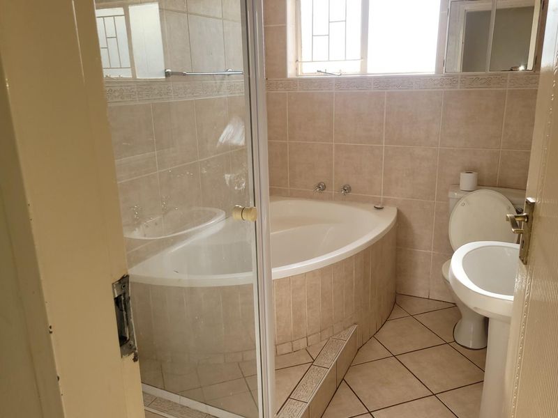 A functional bathroom featuring a corner bathtub, glass shower enclosure, pedestal basin, and toilet, finished with neutral ceramic wall and floor tiles.