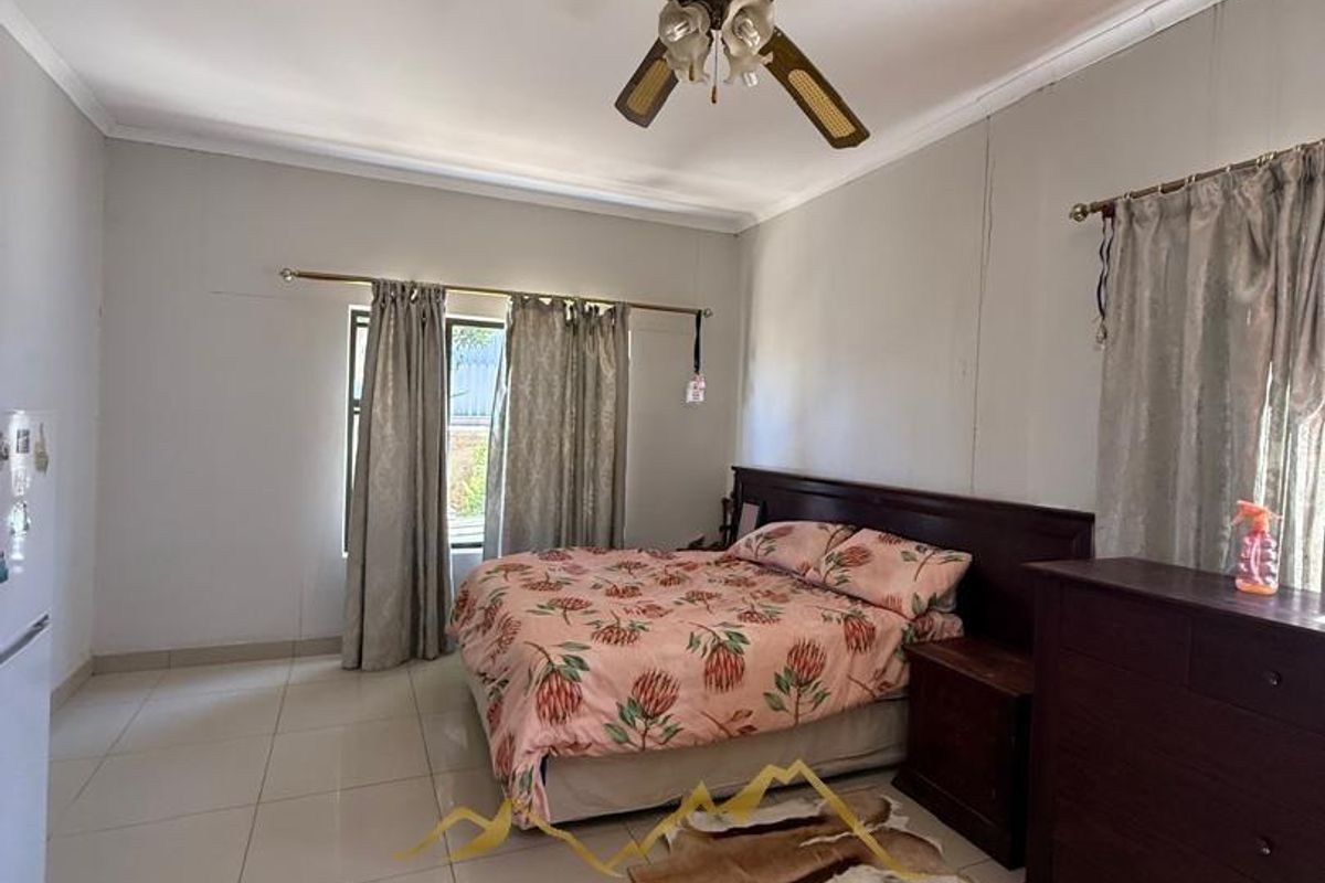 A spacious bedroom featuring tiled flooring, a ceiling fan, and large windows with curtain rods.