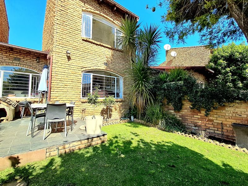 A rear exterior view of a brick townhouse featuring a private garden, a slate patio area, and established landscaping.