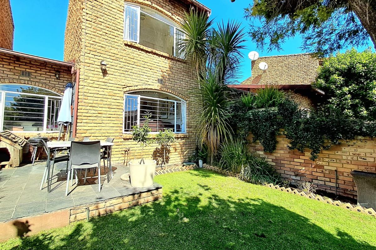 A rear exterior view of a brick townhouse featuring a private garden, a slate patio area, and established landscaping.