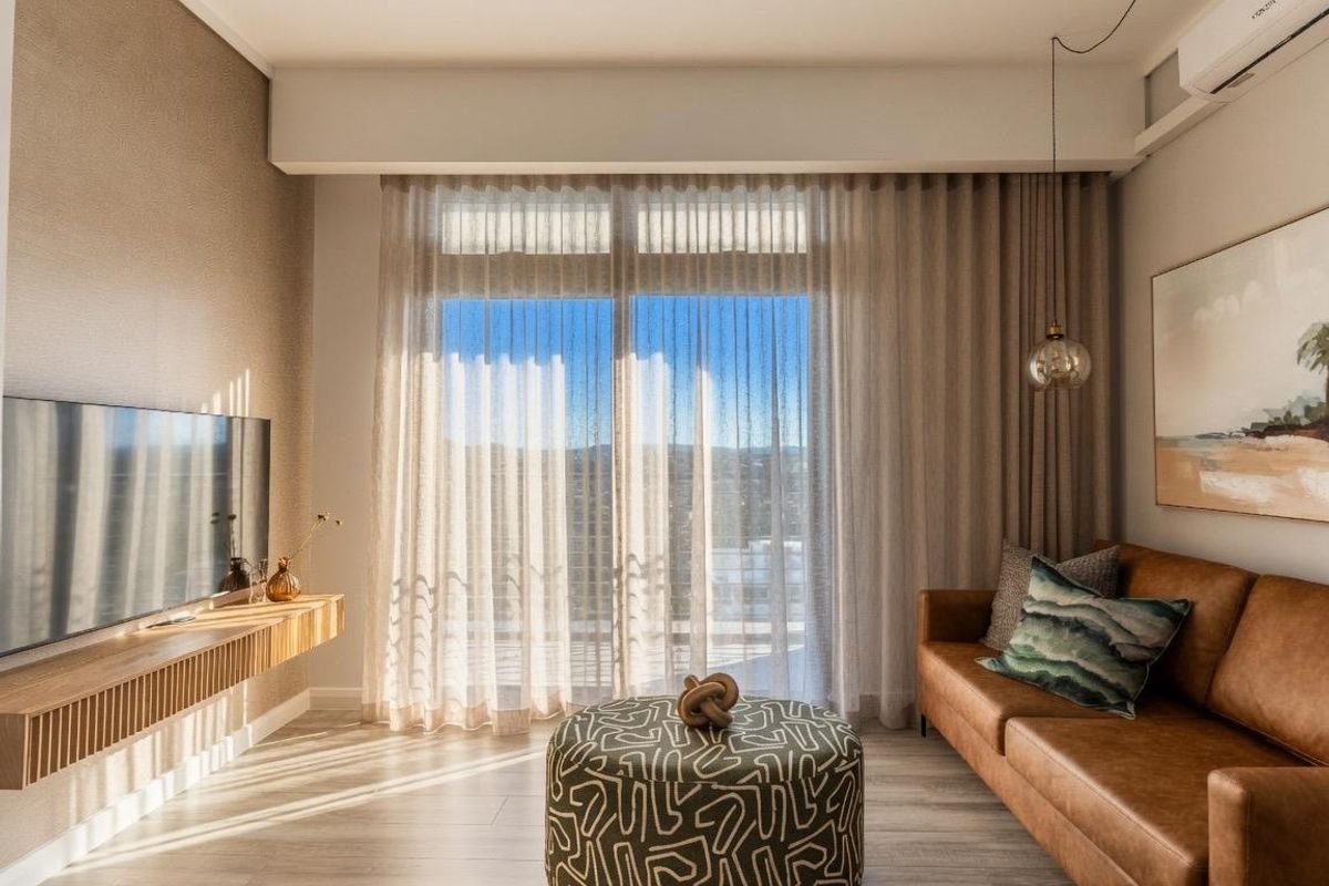 A modern, well-lit living room featuring a wall-mounted timber media console, split-system air conditioning, and large sliding glass doors with sheer curtains.