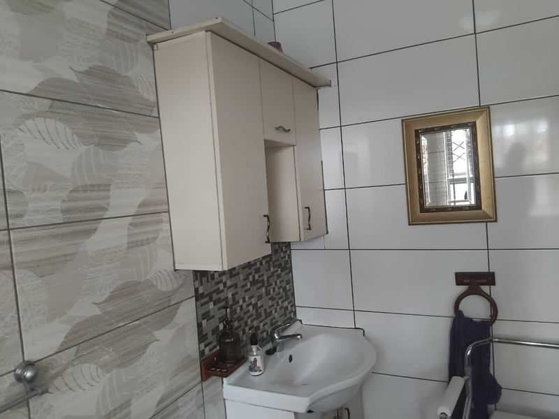 A functional bathroom featuring a wall-mounted vanity cabinet, ceramic basin with chrome mixer tap, and tiled wall finishes.