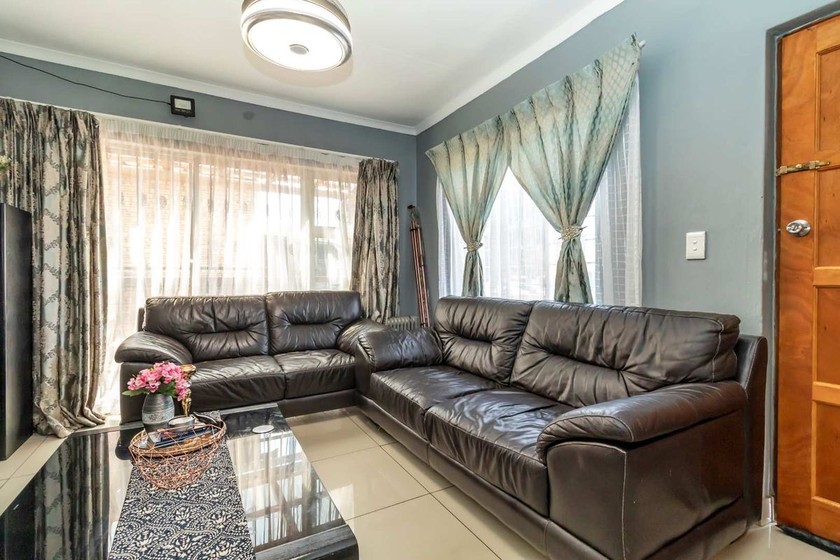 A comfortable living room featuring tiled flooring, a central ceiling light fixture, and natural light through large windows.