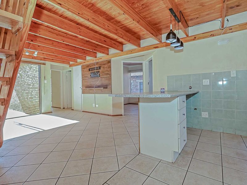 Open-plan living and kitchen area featuring exposed timber ceiling beams, tiled flooring, a central kitchen island, and a built-in media wall.