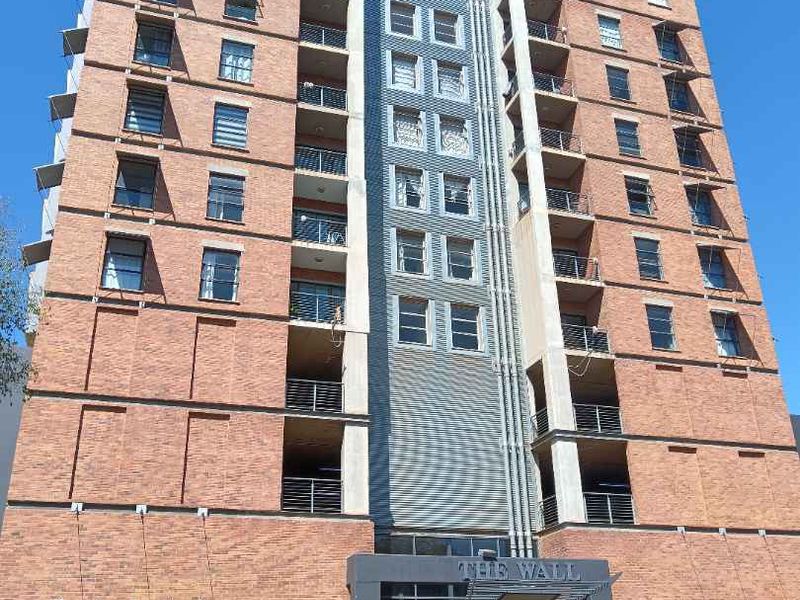 A multi-story brick apartment building featuring balconies, a secure ground-level parking entrance, and a modern main entrance canopy.
