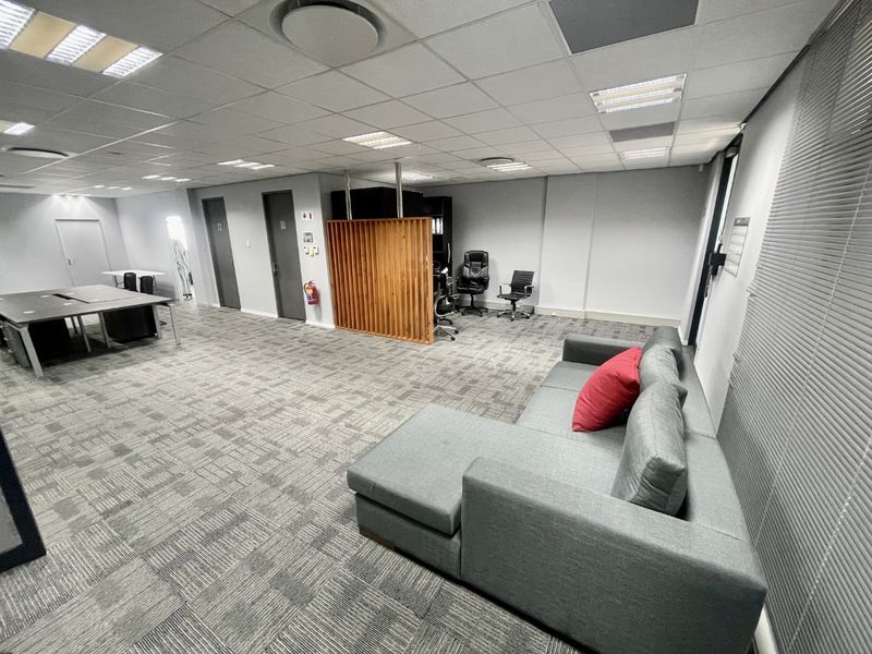 Spacious open-plan office area featuring a suspended ceiling, recessed lighting, carpet tiles, and a decorative wooden slat partition.