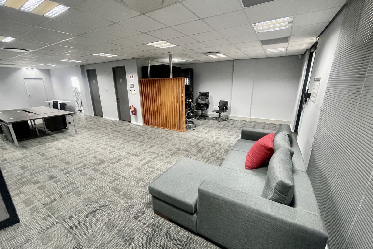 Spacious open-plan office area featuring a suspended ceiling, recessed lighting, carpet tiles, and a decorative wooden slat partition.