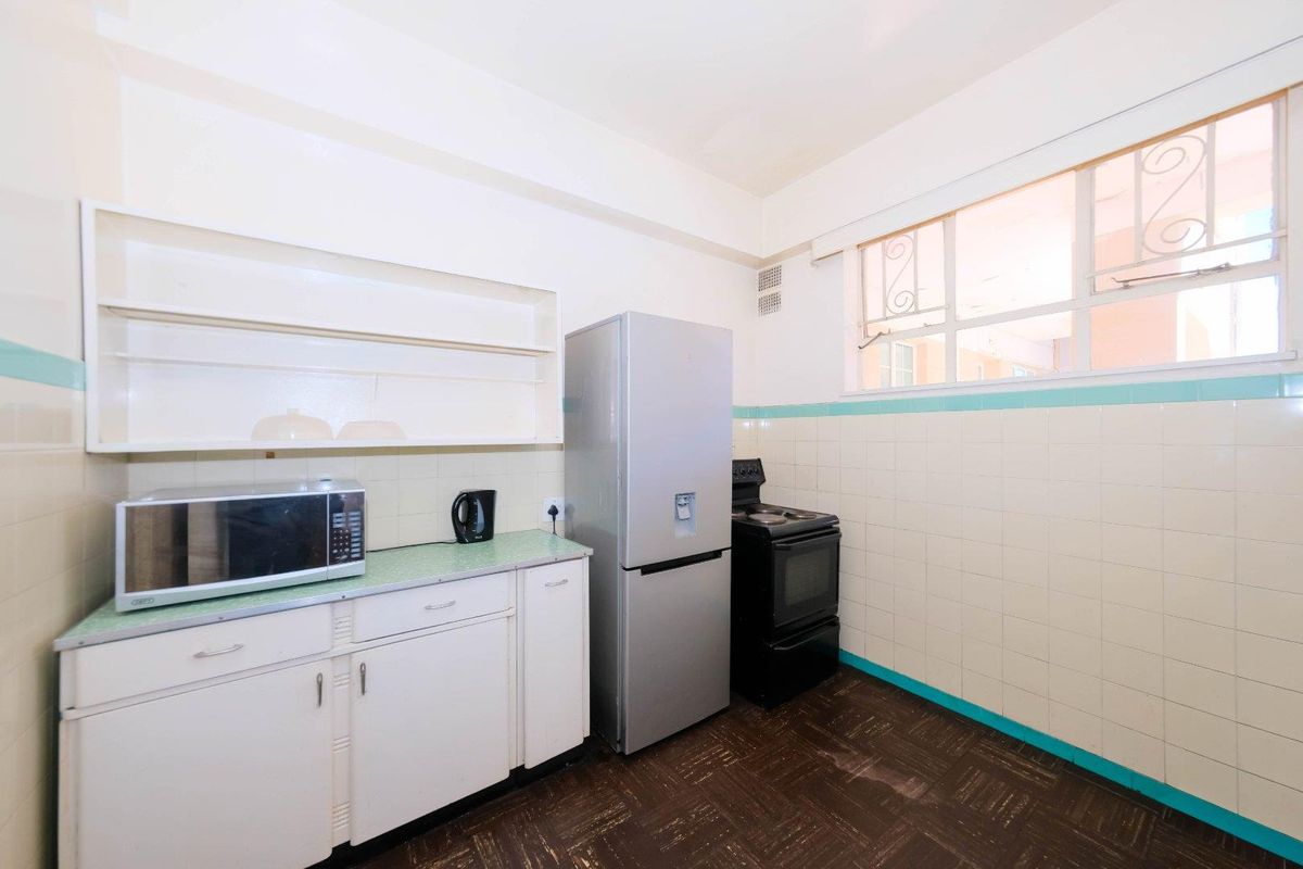 A dated kitchen featuring original cabinetry, tiled splashbacks, and a functional layout with a window providing natural light.