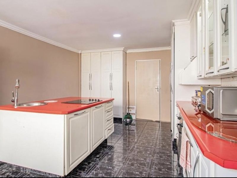 A functional kitchen featuring a central island with a sink and cooktop, ample built-in cabinetry, and dark tiled flooring.