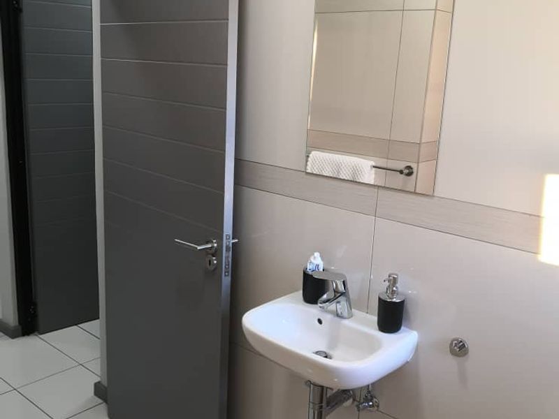 A modern bathroom featuring a wall-mounted basin, chrome fixtures, and neutral wall and floor tiling.