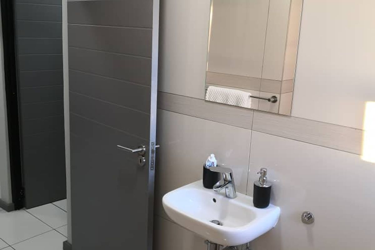 A modern bathroom featuring a wall-mounted basin, chrome fixtures, and neutral wall and floor tiling.