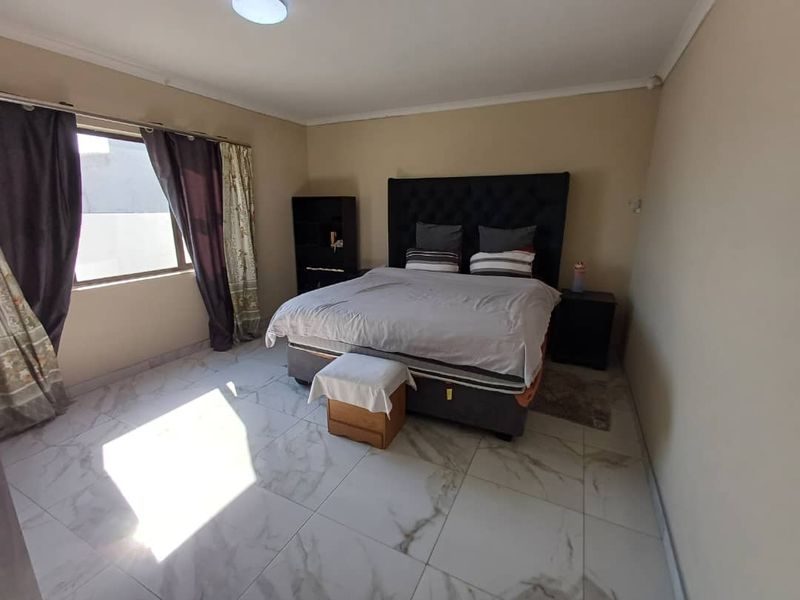 A spacious bedroom featuring large format marble-look floor tiles, neutral wall tones, and a large window allowing for natural light.