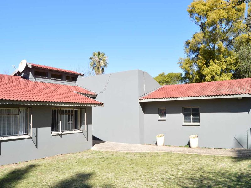 Rear view of the house featuring grey painted walls, terracotta roof tiles, and a paved walkway leading through the garden area.