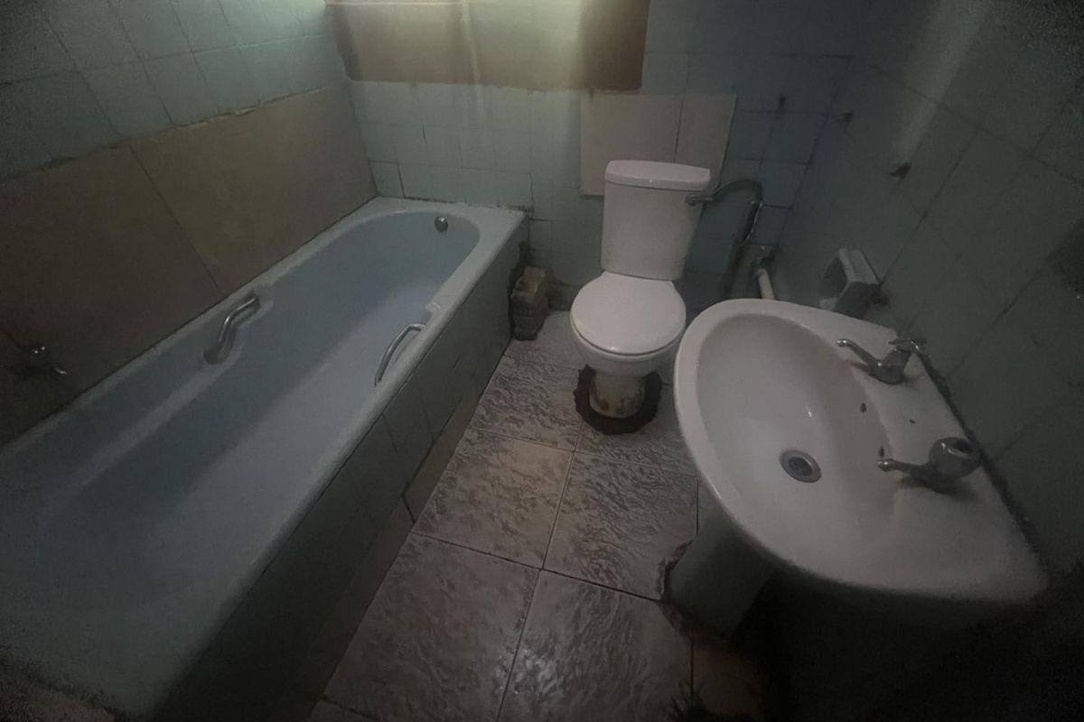 A dated bathroom featuring a bathtub, pedestal basin, and toilet with original wall and floor tiling, requiring significant renovation and modernization.