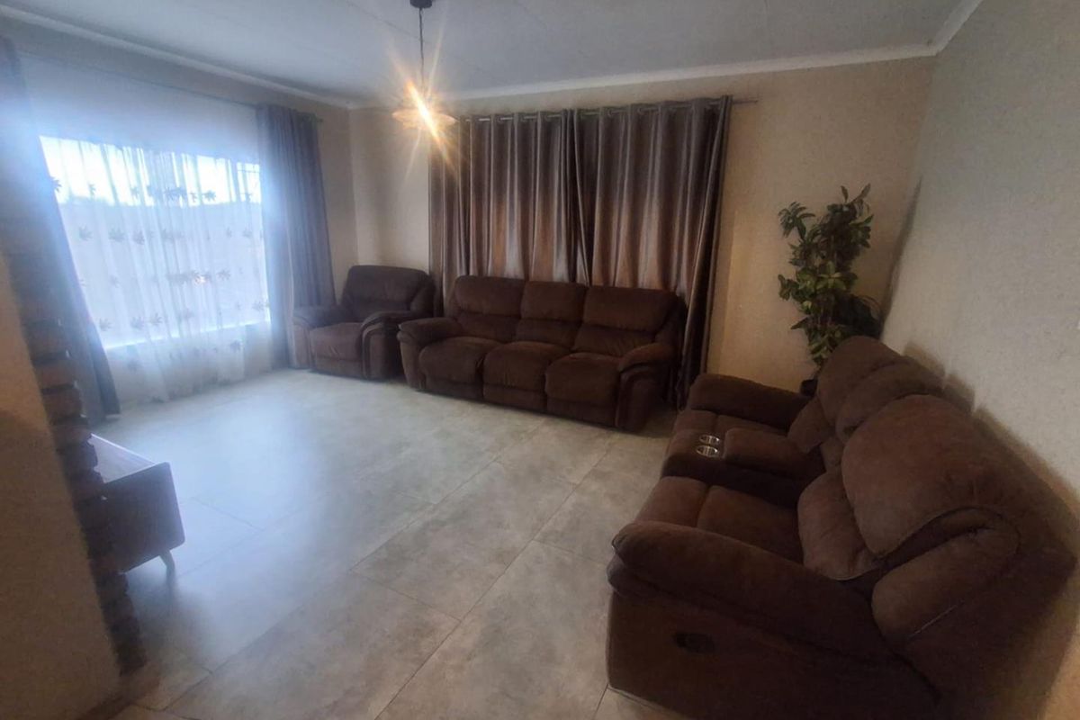 A spacious living room featuring neutral tiled flooring, ceiling cornicing, and large windows with curtain treatments.