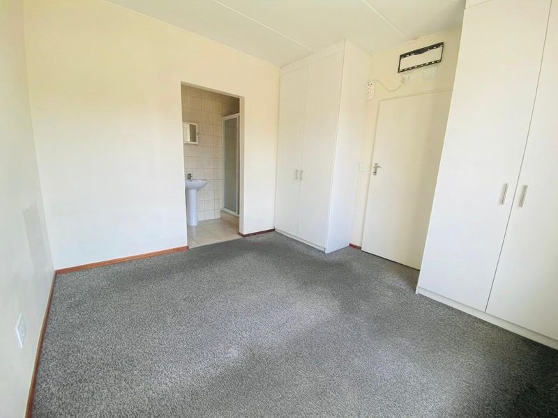 A vacant bedroom featuring built-in cupboards and an attached en-suite bathroom with a pedestal basin and shower enclosure.