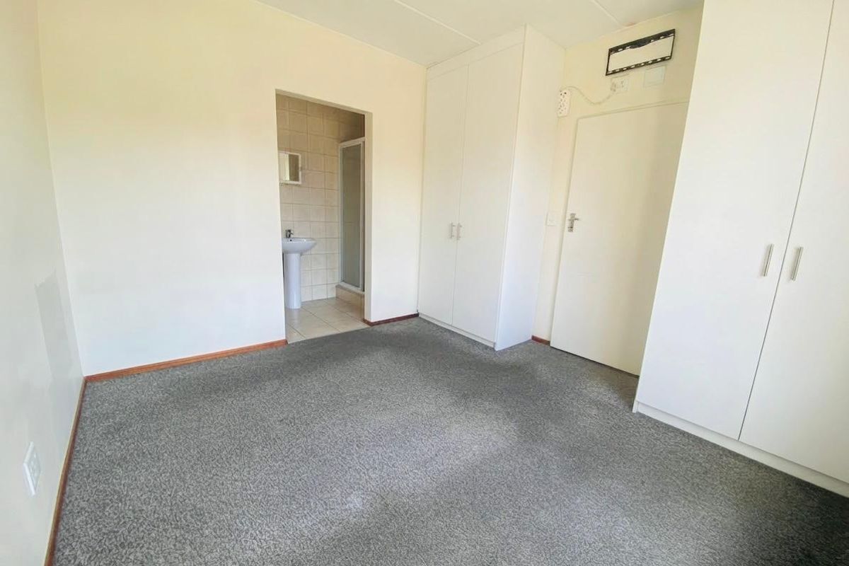 A vacant bedroom featuring built-in cupboards and an attached en-suite bathroom with a pedestal basin and shower enclosure.