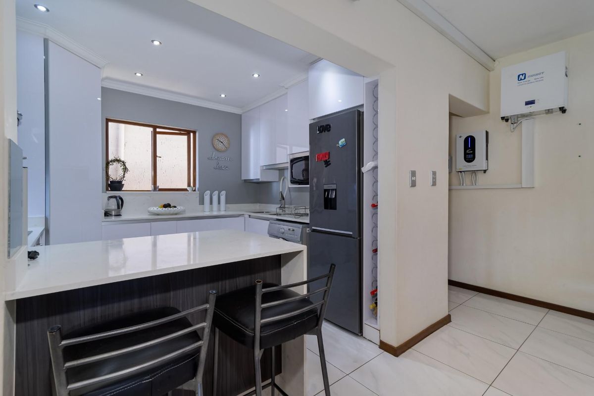 Modern kitchen featuring white cabinetry, stone countertops, a breakfast bar, and integrated energy storage system with a wall-mounted inverter and battery unit.