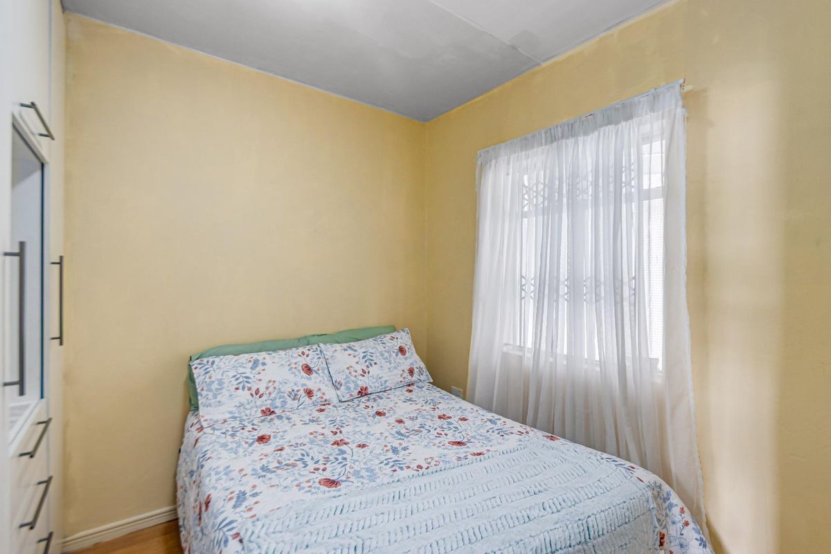 A compact bedroom featuring a built-in wardrobe and a window fitted with a security gate, requiring minor cosmetic updates to the walls and ceiling.