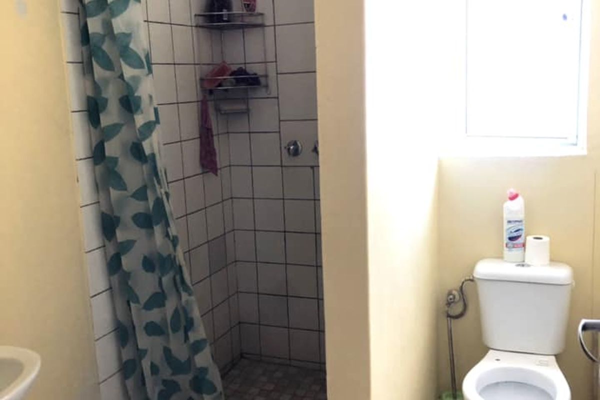 A functional bathroom featuring a walk-in shower with tiled surround, a standard toilet, and a window for natural light.