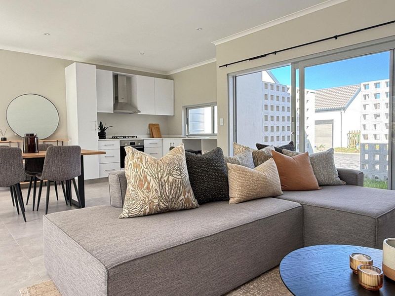 Modern open-plan living and kitchen area featuring sleek white cabinetry, integrated appliances, tiled floors, and large sliding doors opening to the exterior.