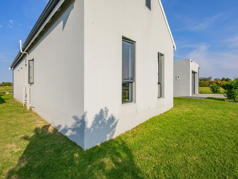 A view of the rear exterior of the modern house, featuring clean white rendered walls, aluminium window frames, and a well-maintained lawn.