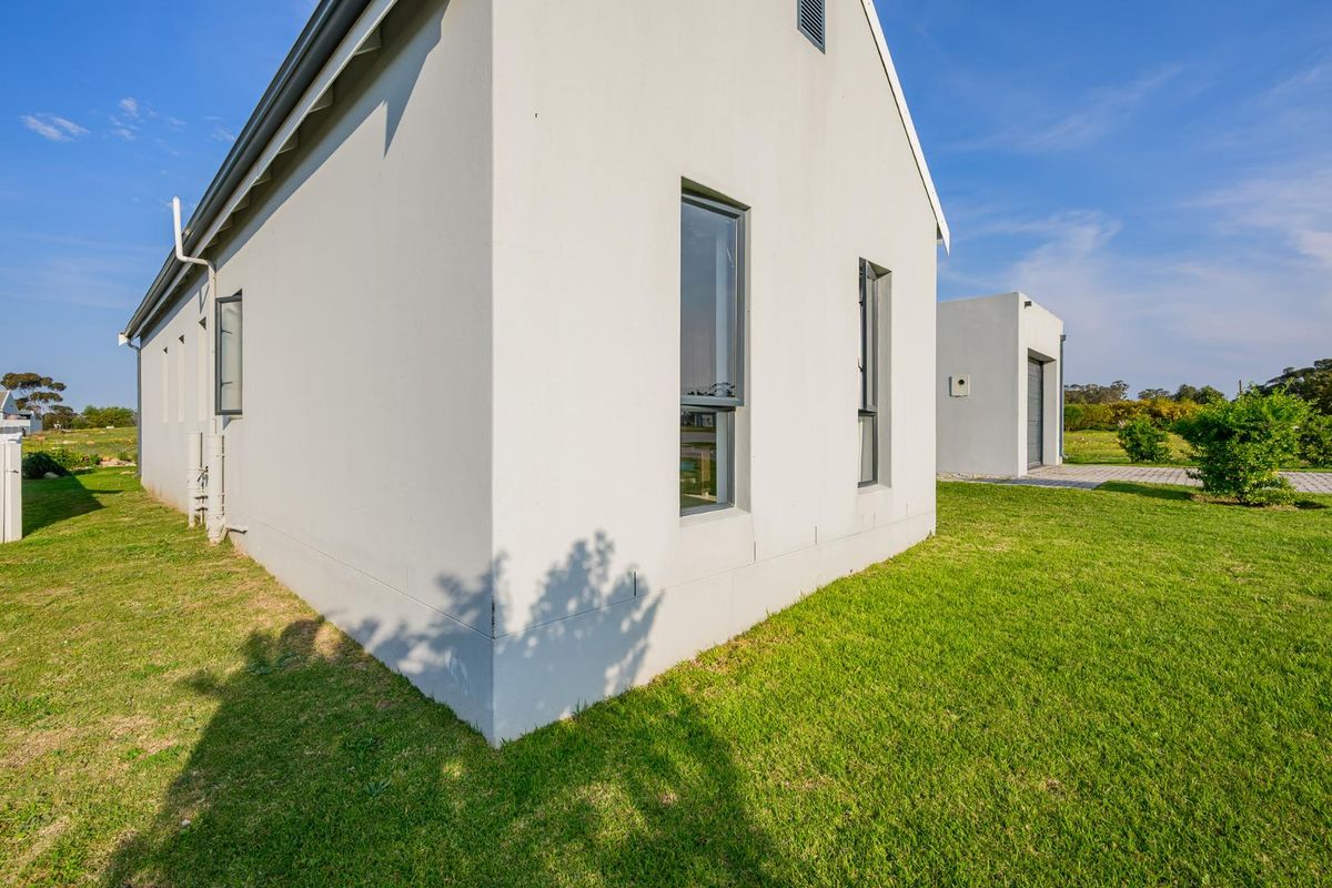 A view of the rear exterior of the modern house, featuring clean white rendered walls, aluminium window frames, and a well-maintained lawn.