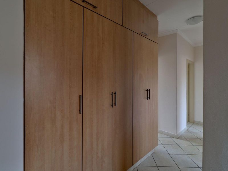 A clean, functional hallway featuring extensive built-in wooden cabinetry for storage and neutral tiled flooring throughout.