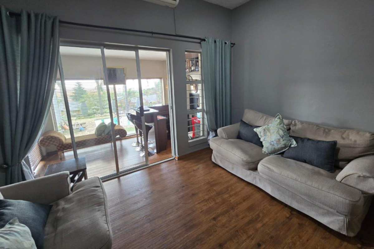 A comfortable living room featuring wood-look flooring, sliding glass doors leading to an outdoor patio area, and a wall-mounted air conditioning unit.