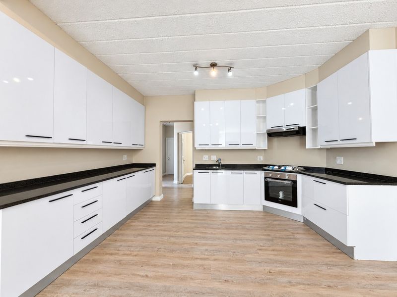 Modern kitchen featuring white gloss cabinetry, black granite countertops, built-in oven, gas hob, and durable laminate flooring in an open, well-lit space.
