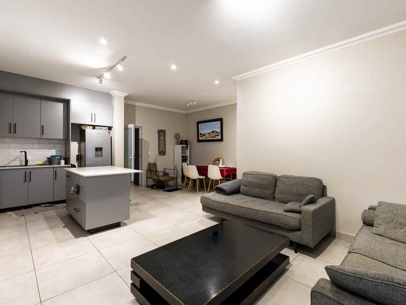 Modern open-plan living area featuring a contemporary kitchen with grey cabinetry, a central island, subway tile backsplash, and neutral tiled flooring throughout.