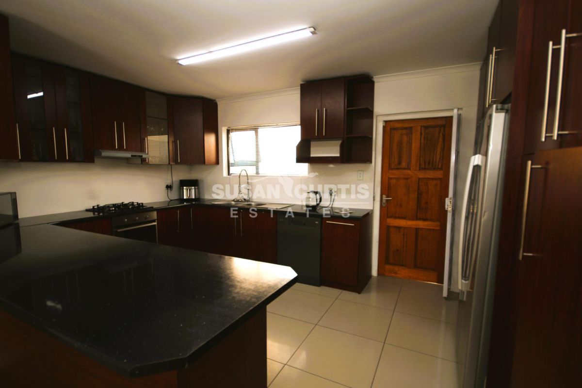 A functional kitchen featuring dark wood cabinetry, black granite countertops, a gas hob, and tiled flooring, providing a practical workspace for cooking and preparation.