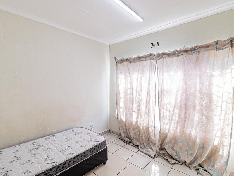 A bedroom featuring tiled flooring and a ventilation grille, currently requiring cosmetic updates to the wall finishes.