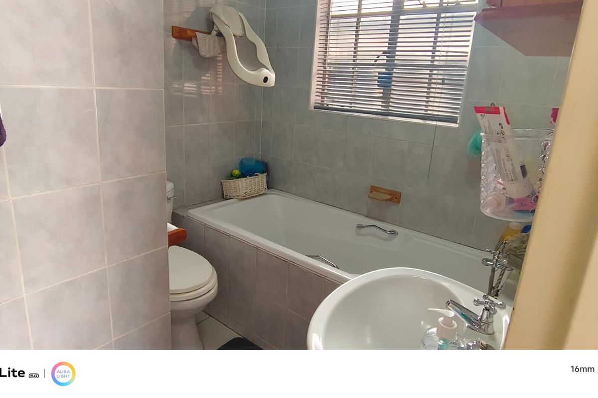 A functional bathroom featuring a bathtub, toilet, and pedestal basin with tiled wall finishes and window blinds.