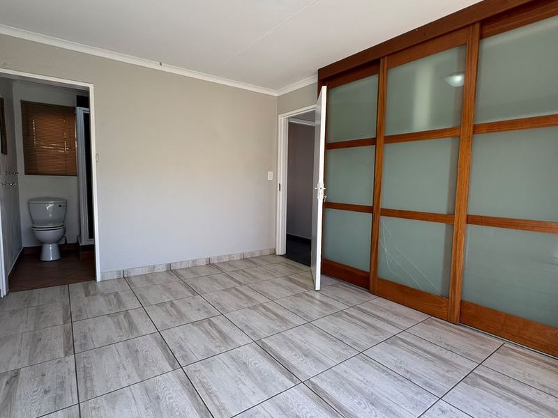 Empty bedroom featuring tiled flooring and a large built-in sliding door wardrobe with a cracked glass panel, leading to an en-suite bathroom.