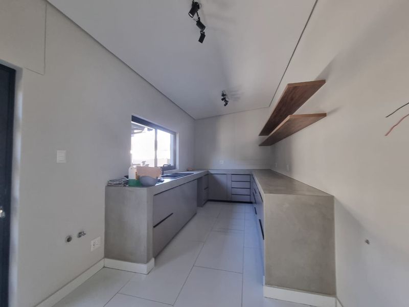 Modern kitchen featuring minimalist concrete cabinetry, floating wooden shelving, and sleek tiled flooring in a clean, contemporary design.
